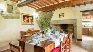 A rustic dining room with a stone fireplace, wooden beams, and a table set for a meal. - Ar-d077-lper0at - La Torretta 10 (Cortona)