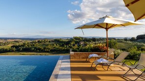 A poolside area with a view of a hilly landscape, including houses and vineyards.