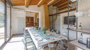 Un'area pranzo moderna con un tavolo lungo apparecchiato per un pasto, sedie trasparenti e un angolo cottura sullo sfondo.