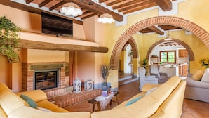 Uma sala de estar ampla com lareira, assentos confortáveis e cozinha aberta visível através de um arco.