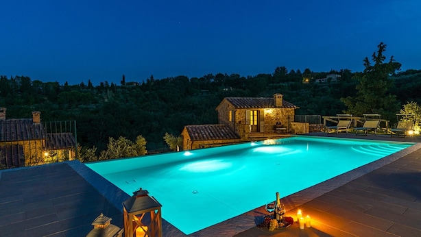 Piscina com uma casa de pedra e espreguiçadeiras ao fundo.