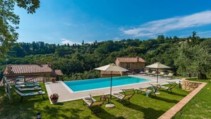 A pool area with lounge chairs and umbrellas, surrounded by stone buildings and lush greenery.
