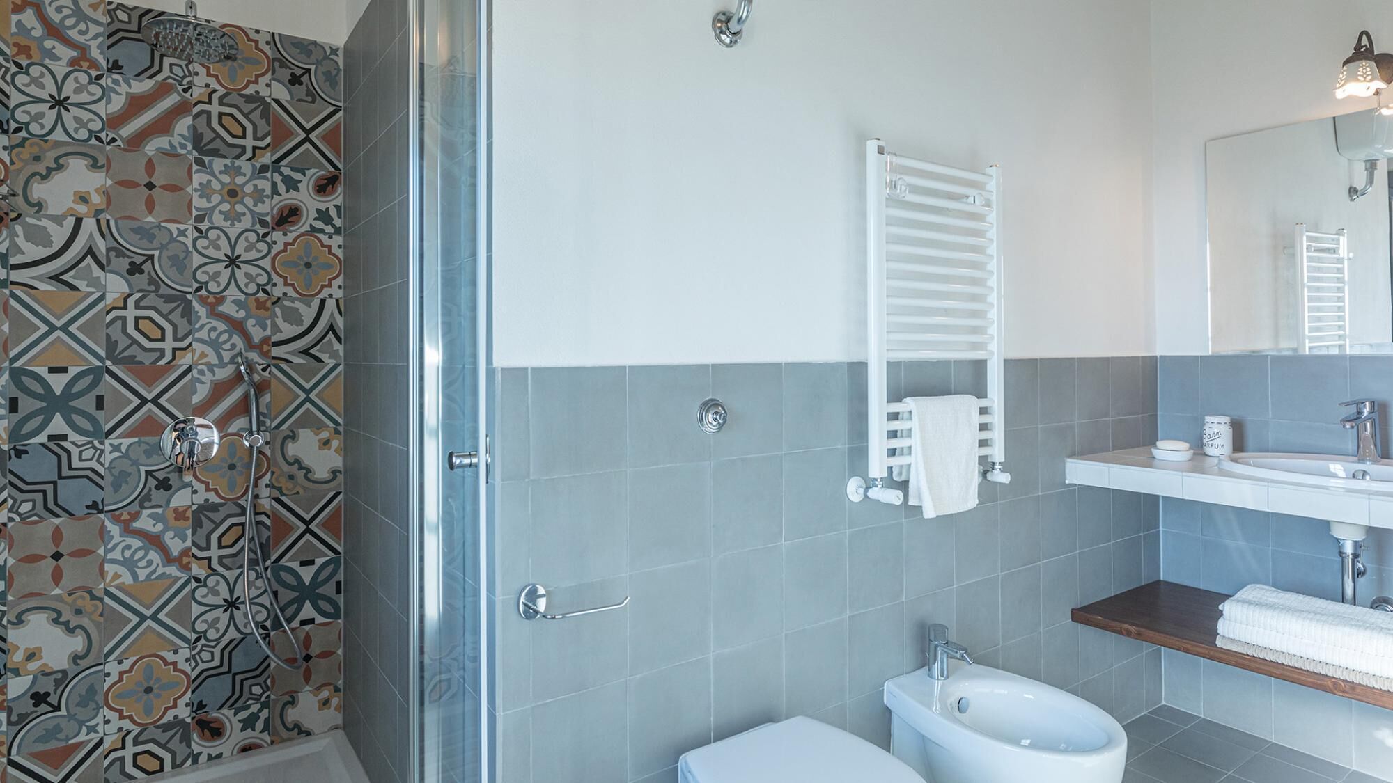 A bathroom with a shower, toilet, bidet, and a sink with a mirror.
