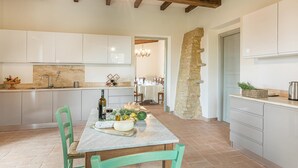 A modern kitchen with white cabinets, a marble countertop, and a dining table set with food and drinks. - Il Colle Di Donna Ilaria 16 (Buonconvento)