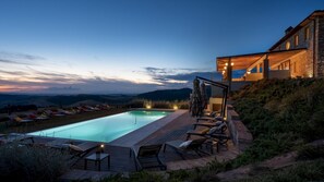 A pool area with lounge chairs and a wooden deck, surrounded by a stone wall and overlooking a scenic landscape. - Il Poggiarellone 18 (Volterra)