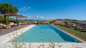 A rectangular pool with clear blue water, surrounded by lounge chairs and a pergola. - Il Poggiarellone 18 (Volterra)
