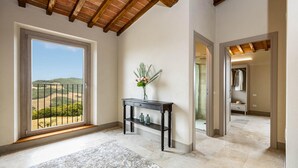 Amplia habitación con un gran ventanal que ofrece vistas a un paisaje montañoso. Una consola de madera oscura con un florero está colocada contra la pared.