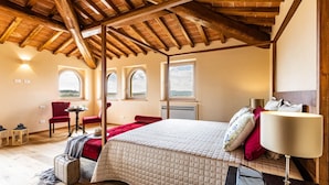 Un dormitorio con techo de madera, una cama con cubrecama acolchado, una mesita de noche, una lámpara y vistas del exterior a través de ventanales arqueados.