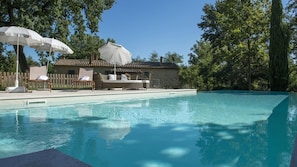 A swimming pool with lounge chairs and umbrellas, surrounded by trees and a stone building.