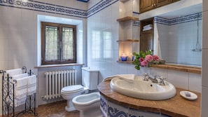 A bathroom with a white toilet, a bidet, a sink with a mirror above, and a window with lace curtains.