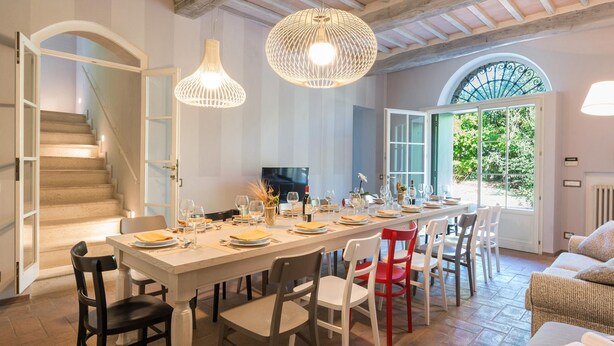 A dining area with a long table set for a meal, a TV, and a staircase leading to another level.