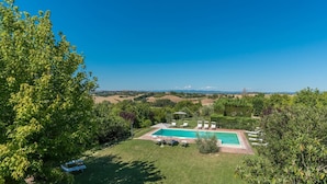 A swimming pool with lounge chairs and a table, surrounded by lush greenery and a view of distant hills.