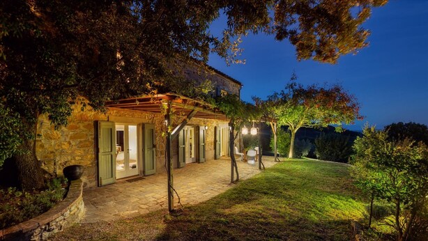 A stone house with a covered patio, outdoor seating, and a well-lit garden at dusk. - Cinque Cipressi 8 in Montecatini Val di Cecina (Montecatini Val di Cecina)