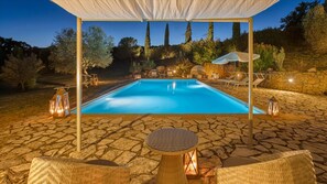 An outdoor pool area with a covered seating area, stone flooring, and a fire feature.
