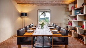 A dining room with a long table set for six, surrounded by leather chairs, with a view of greenery outside. - Cinque Cipressi 8 in Montecatini Val di Cecina (Montecatini Val di Cecina)