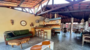 A spacious indoor area with a high ceiling, a wooden bar counter, a green sofa, and a dining area with tables and chairs.