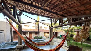 A hammock under a wooden pergola, a small pool, and a patio area with a chair and table.