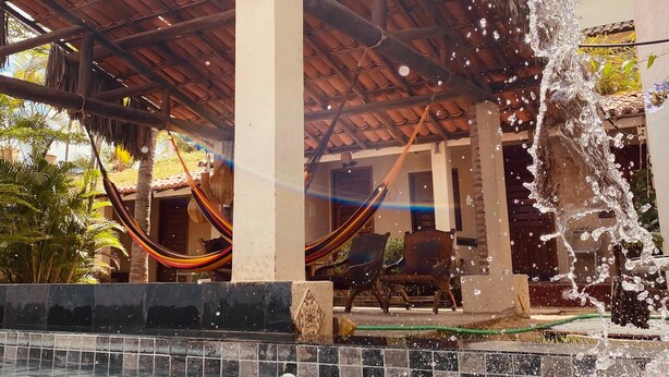 A pool area with a water feature, a hammock, and a covered seating area.