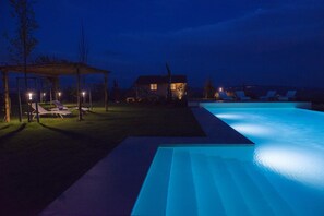 A nighttime swimming pool area with lounge chairs and a gazebo. - Rosa Dei Venti 8 in Fabro (Fabro)