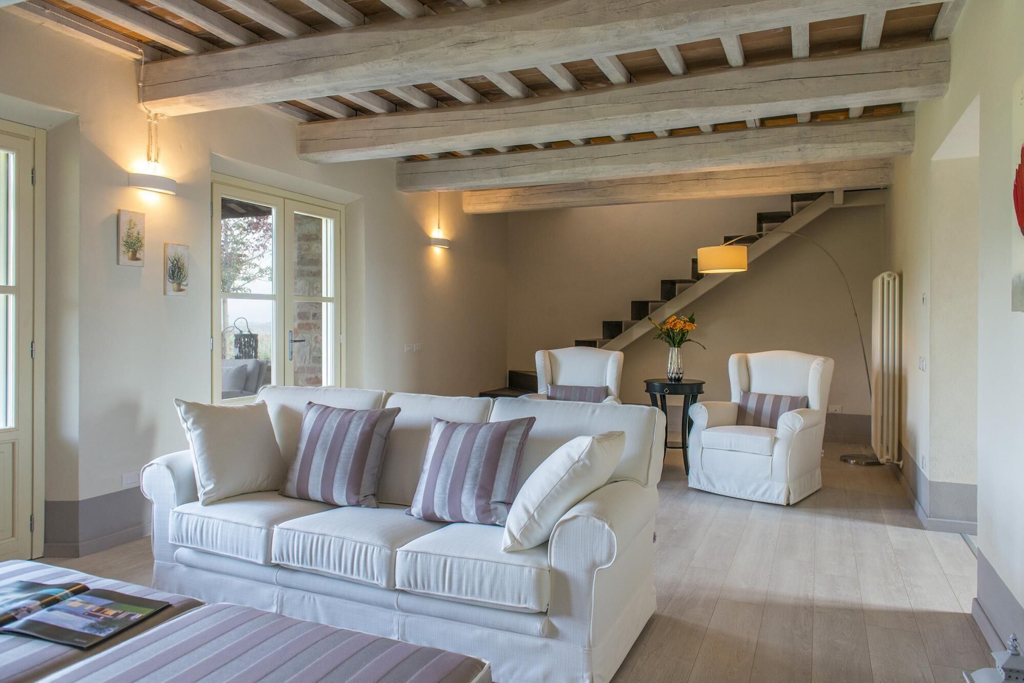 A spacious living area with a white sofa set, a coffee table, and a staircase leading to an upper level.
