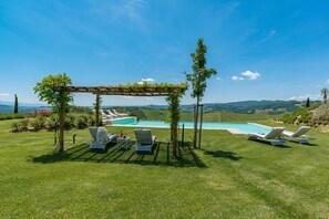 A poolside area with lounge chairs and a pergola, surrounded by a grassy lawn and a view of rolling hills. - Rosa Dei Venti 8 in Fabro (Fabro)