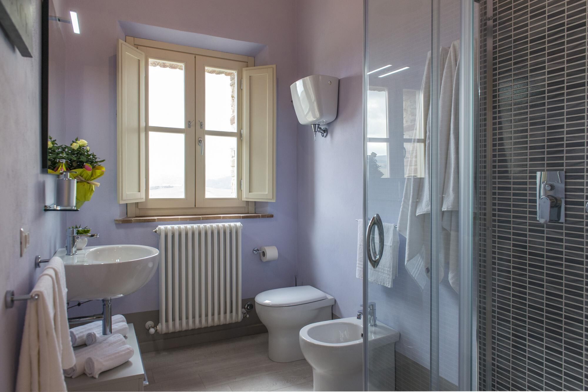 Une salle de bain avec deux lavabos, des toilettes, une douche et une fenêtre avec des rideaux.