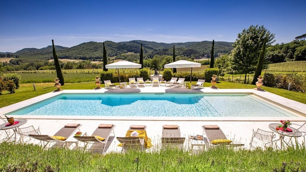 A rectangular swimming pool with lounge chairs and umbrellas, surrounded by lush greenery and hills in the background. - Le Querce Dei Medici 12 2 (Scarperia e San Piero)