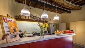 A kitchen with a marble countertop, hanging pendant lights, a vase with flowers, and a fruit bowl. - Le Querce Dei Medici 12 2 (Scarperia e San Piero)