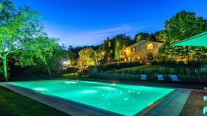 A rectangular swimming pool with a stone border, surrounded by a well-maintained lawn and trees.