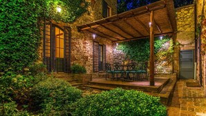 A stone building with ivy-covered walls, a wooden pergola, and a table with chairs in the center.