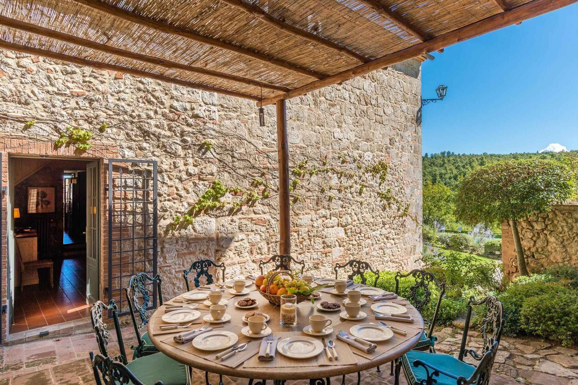 A round table set for a meal with a stone wall backdrop, outdoor seating, and a view of a mountainous landscape.