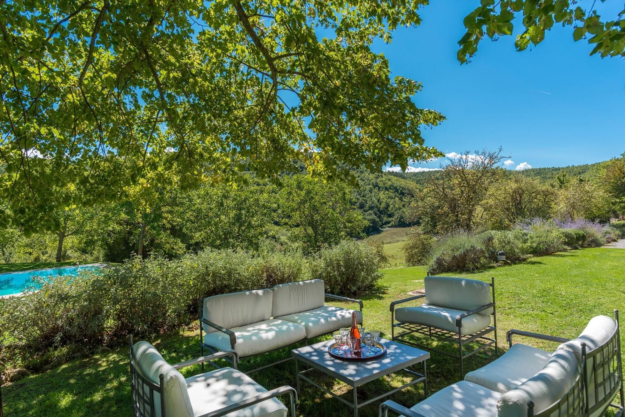 A patio with outdoor furniture, a pool, and a view of a lush green landscape.