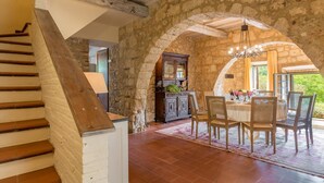 A rustic dining area with stone walls, a wooden staircase, and a chandelier.