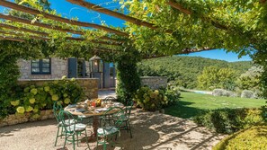 An outdoor patio with a table set for dining, surrounded by greenery and a stone wall. - Muffato 6 in Sarteano (Sarteano)