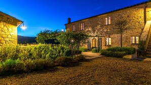 A stone building with a gravel courtyard, a wooden fence, and a well-lit entrance. - Muffato 6 in Sarteano (Sarteano)