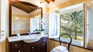 A bathroom with a large mirror, wooden vanity, and a window with a view of trees.