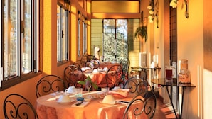 Un coin repas baigné de lumière, avec une table dressée pour deux personnes, agrémenté d’une nappe, de chaises et d’une petite table d’appoint sur laquelle se trouve un bocal en verre.