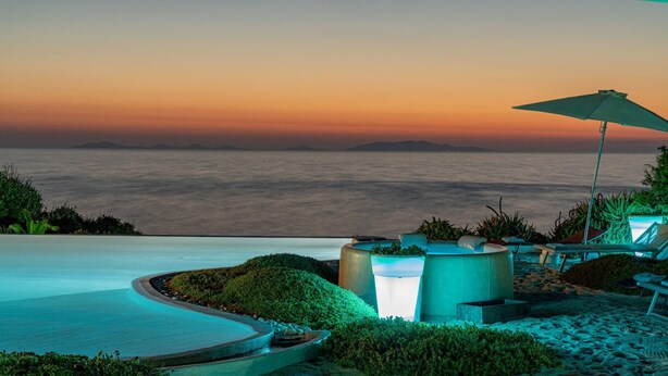 A poolside area with lounge chairs and an umbrella, overlooking a body of water at sunset. - Villa Ambra 10 in Sorso (Castelsardo)