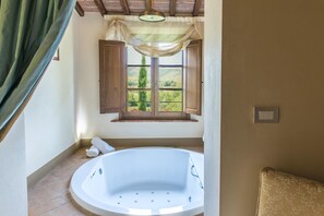 A bathroom with a bathtub, a window with wooden shutters, and a towel on the floor.