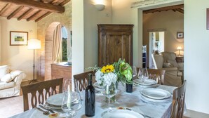 Un coin repas avec une table dressée pour quatre personnes, entourée de chaises en bois. On aperçoit, au fond, une armoire en bois et une lampe.