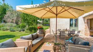 An outdoor patio with wicker furniture, a table, and a large umbrella. - San Francesco 12 in Sarteano (Cetona)