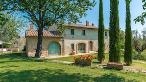A stone building with a tiled roof, arched windows, and a well-maintained lawn with flower beds. - San Francesco 12 in Sarteano (Cetona)