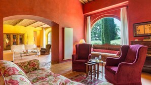 A spacious living room with a fireplace, a sofa, armchairs, and a view of the outdoors. - San Francesco 12 in Sarteano (Cetona)