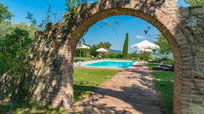 A swimming pool with a brick archway, surrounded by grass and trees. - San Francesco 12 in Sarteano (Cetona)