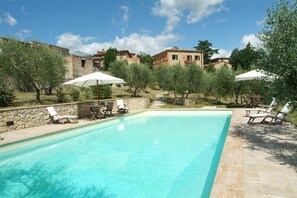 A swimming pool with lounge chairs and umbrellas, surrounded by stone walls and trees. - Villa Angelini 14 7 (Murlo)