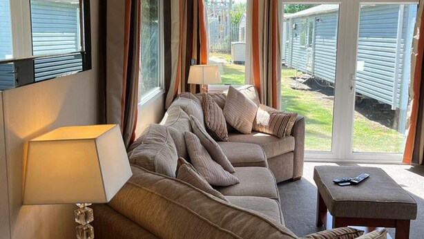 Una sala de estar acogedora con un sofá, una mesita de centro y una lámpara. Se ve una ventana con cortinas y vistas al exterior.