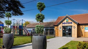 Un edificio con un cartel que dice 'WELCOME', un parque infantil y macetas grandes.