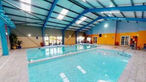 Una piscina interior con agua cristalina azul, rodeada de paredes de azulejos y un techo alto con vigas azules.