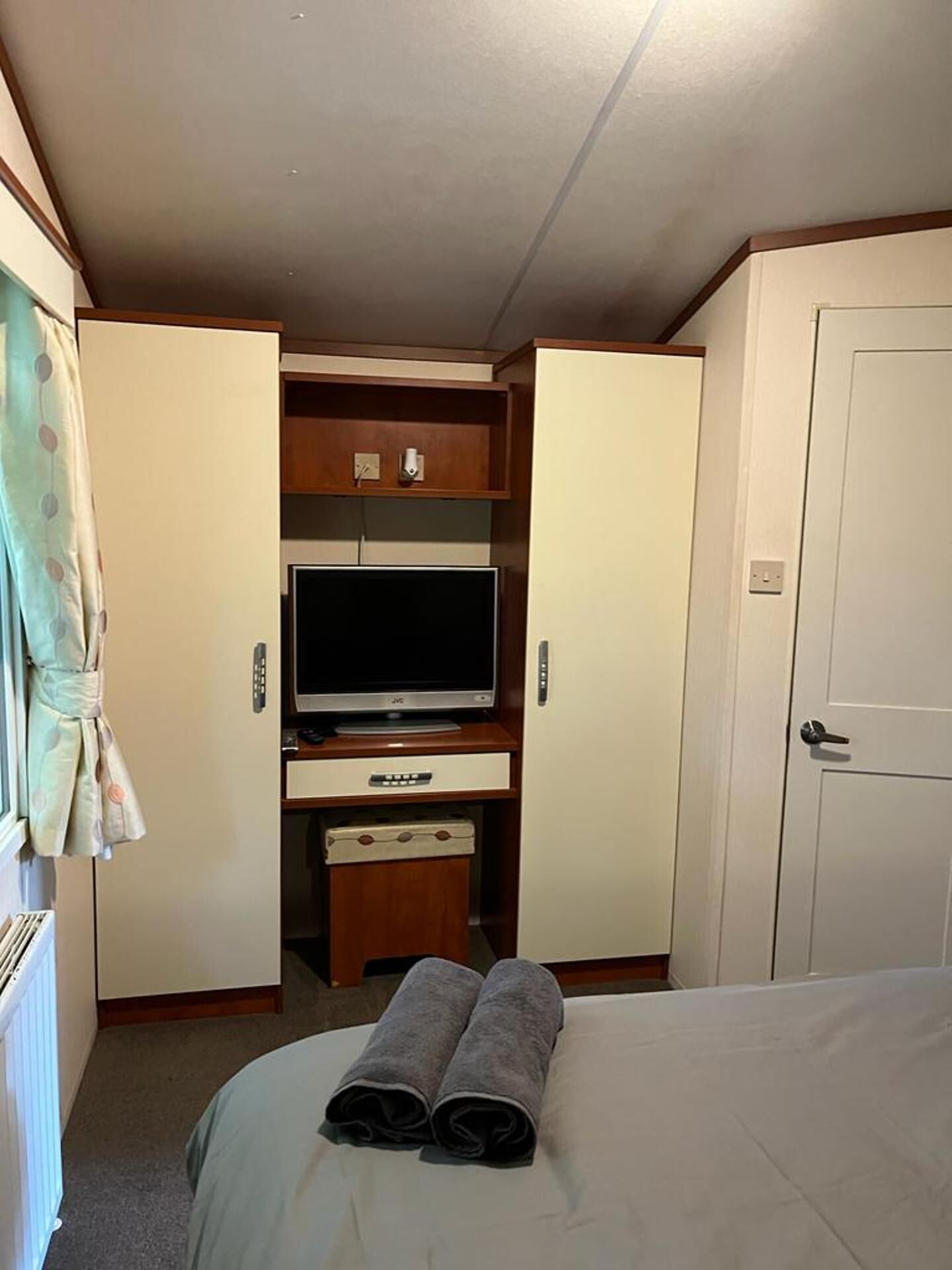 A compact hotel room with a bed, a TV on a wooden stand, a wardrobe, and a door.