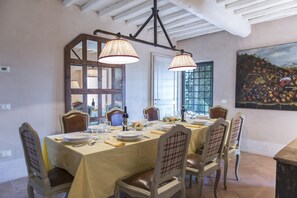 Une salle à manger avec une table dressée pour six personnes, des chaises en bois et un tableau représentant des fruits accroché au mur.